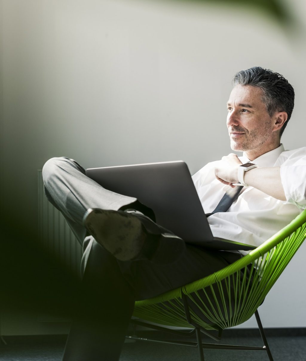 Smiling businessman with laptop sitting in an armchair